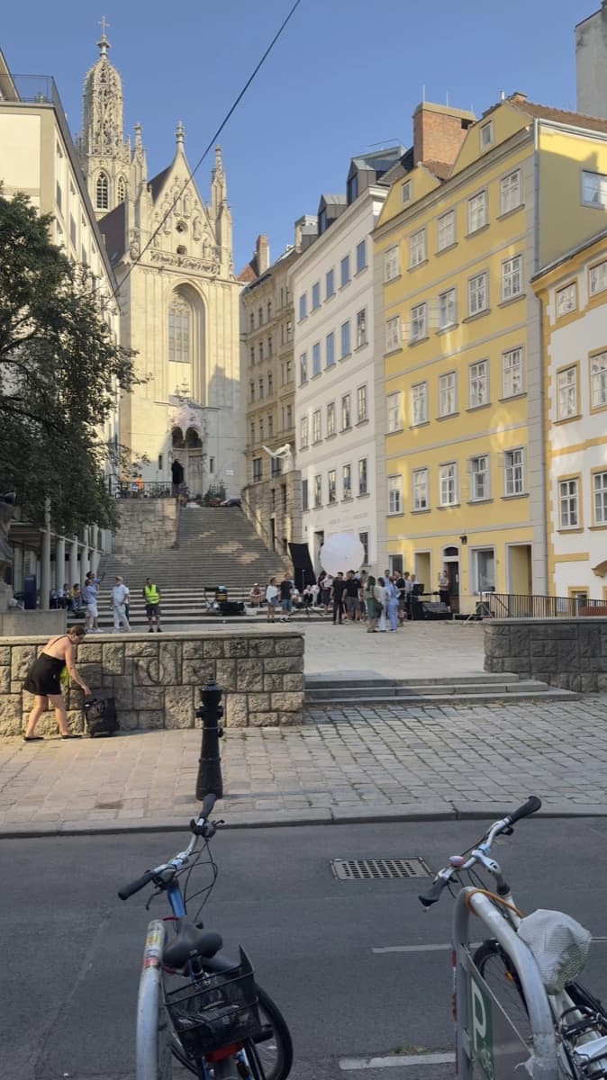 A church at the top of a flight of steps in Vienna, with yellow houses beside it and bikes parked in front
